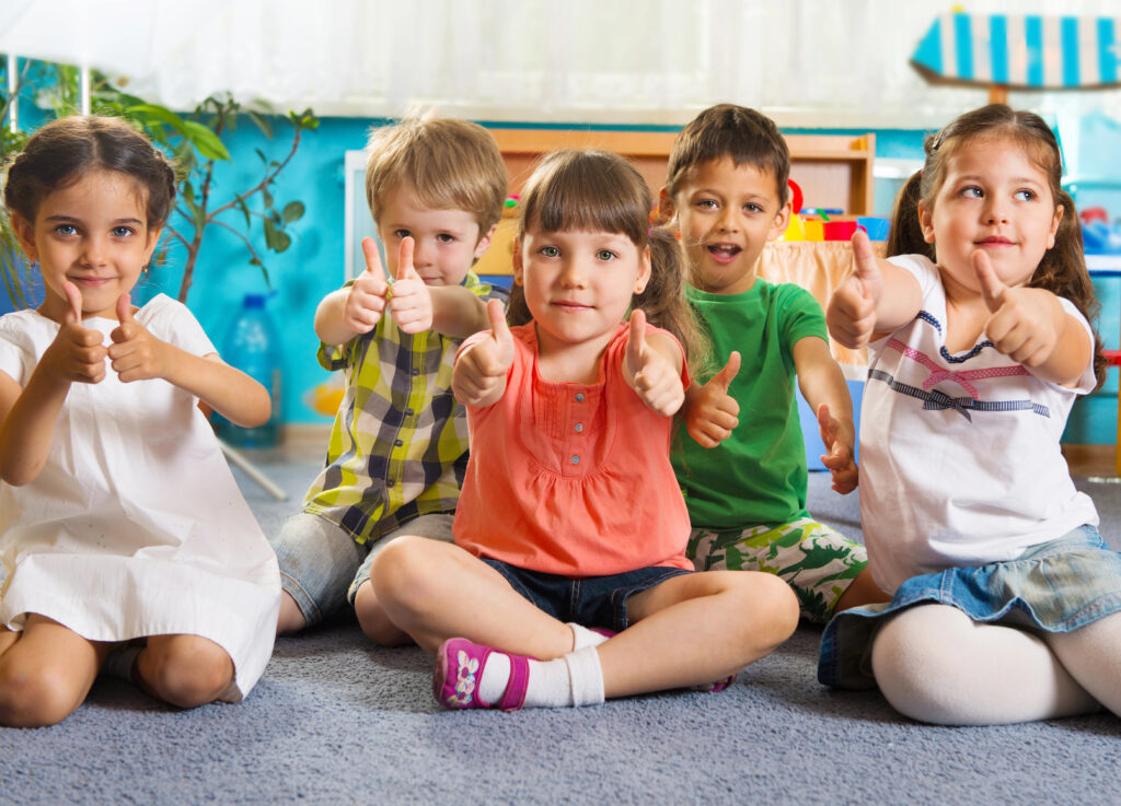 Group of smiling children sitting on the floor giving thumbs up